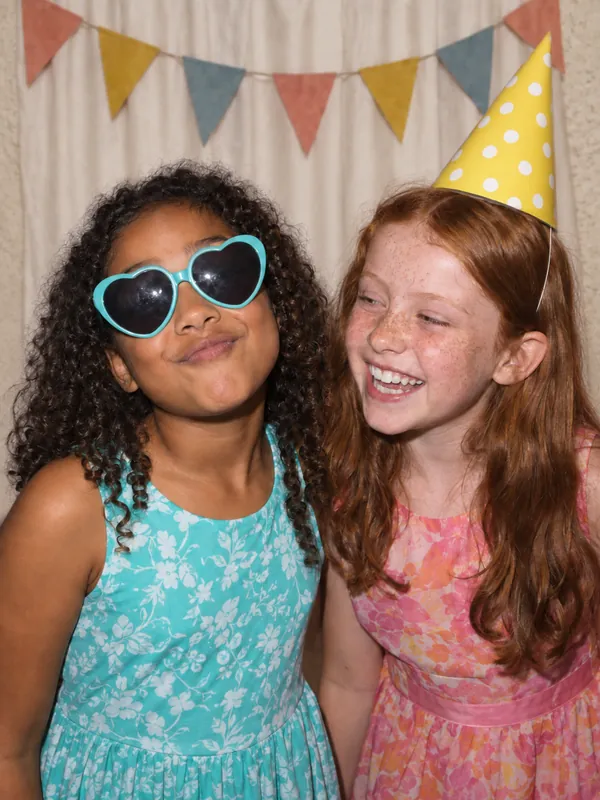 Best friends in heart glasses and a party hat at an LA kids party photobooth
